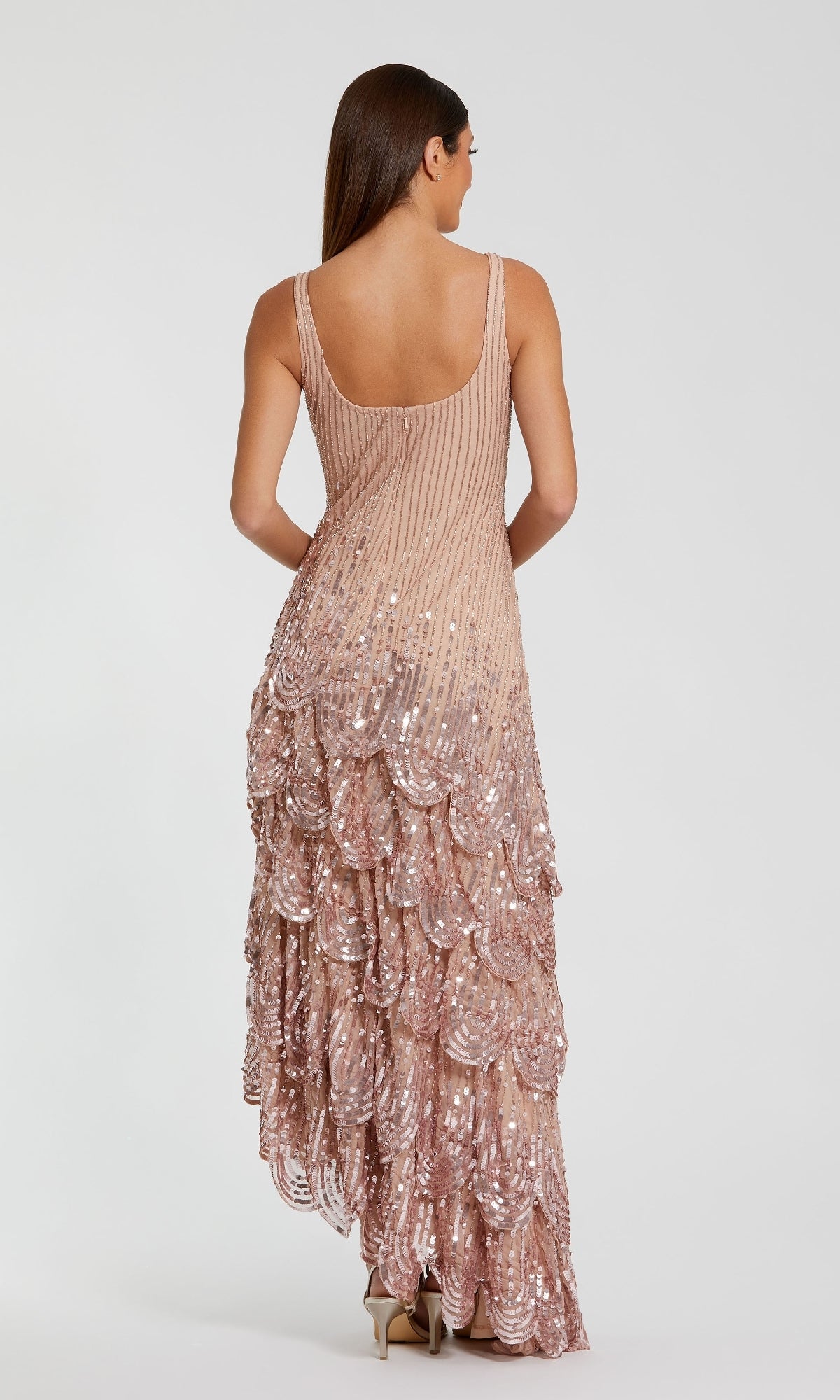 A woman faces away, wearing the Mac Duggal 94195 Long Formal Dress—a sleeveless, floor-length blush pink gown with sequins and scalloped layers on the skirt.
